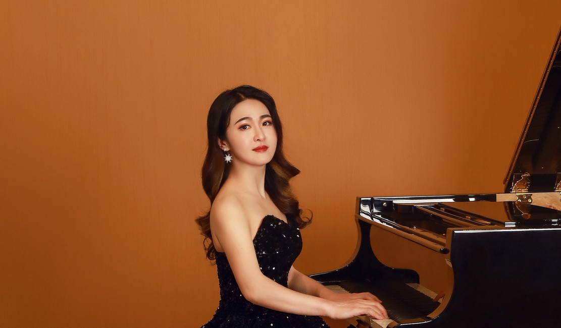 Lishan Xue dressed in a black dress sitting at a grand piano.